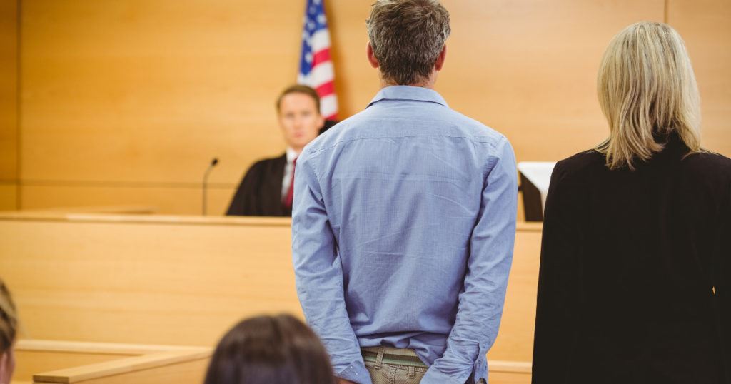 man in handcuffs with attorney before a judge