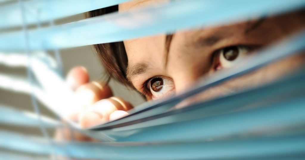 man peaking out from blinds