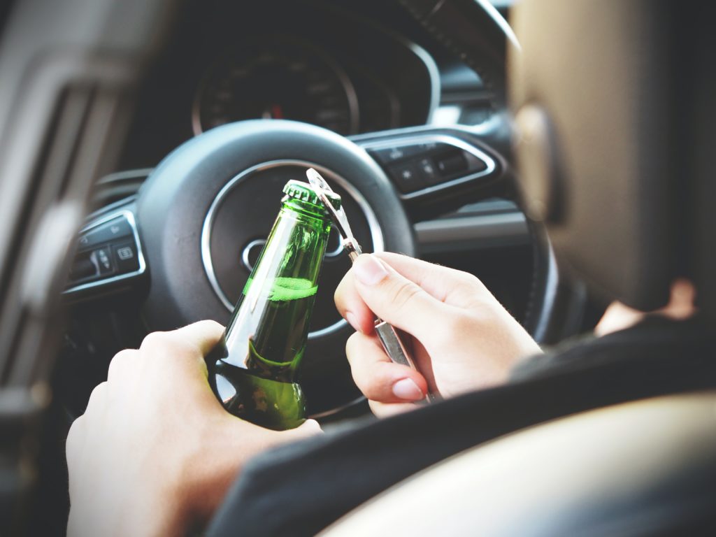 person opening beer bottle in car